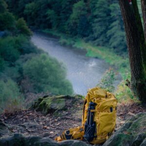 Yellow backpack rests on rocky ground overlooking river.